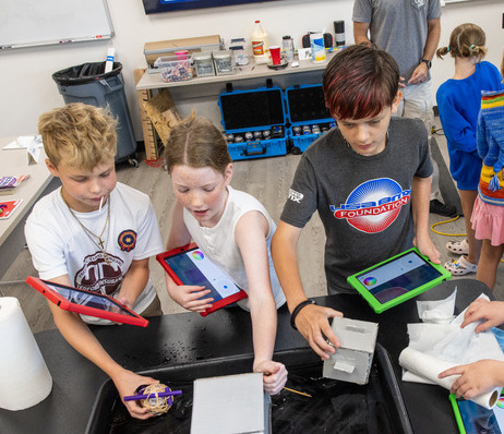 Kids engaging in a STEM camp activity with tablets and water.