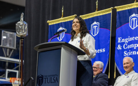 UTulsa alumna speaks at podium; "The University of Tulsa" logo visible.