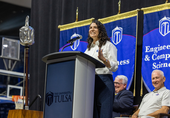 UTulsa alumna speaks at podium; "The University of Tulsa" logo visible.