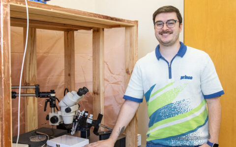 Biological science student with microscope at Air Force research facility studying insect vision.
