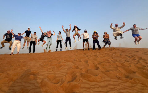 Group of people jumping in the air on a sand dune at a UTulsa Jumpstart event.