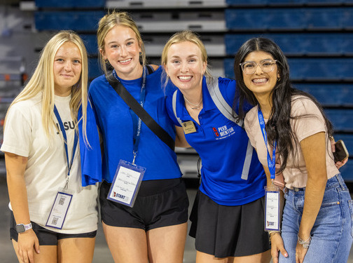 Four smiling students at New Student Orientation, wearing name tags and posing for a photo.