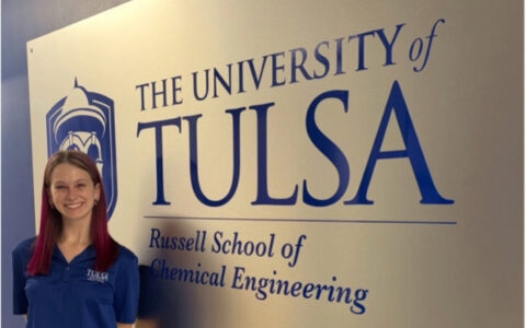 University of Tulsa chemical engineering student stands in front of school signage.