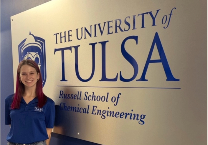 University of Tulsa chemical engineering student stands in front of school signage.