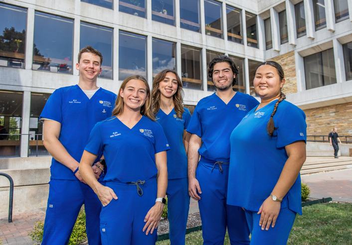 UTulsa nursing students in blue scrubs outside the health and natural sciences building.
