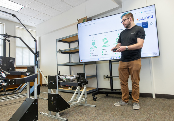 Man presenting Green UAS AUVSI drone cyber security review, with robotics vulnerability testing equipment.