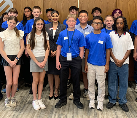 Group photo of diverse students with a woman in business attire at a summer camp workshop.