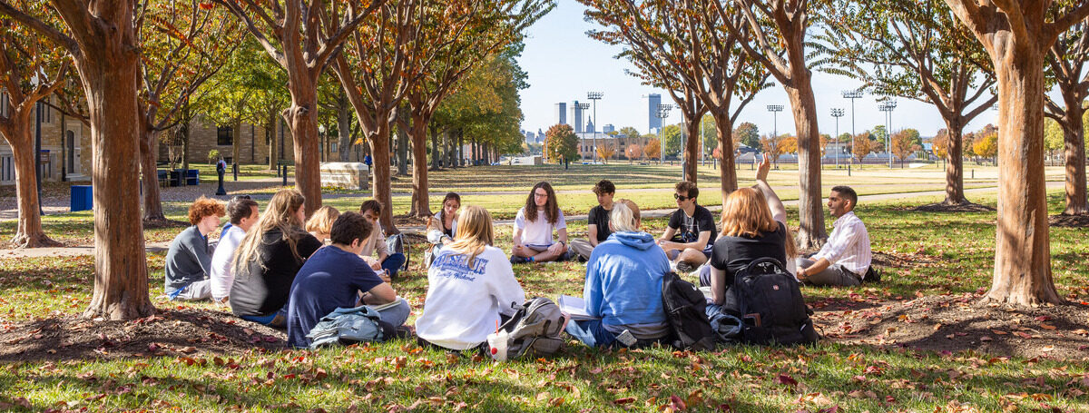 Students in outdoor class circle on campus lawn