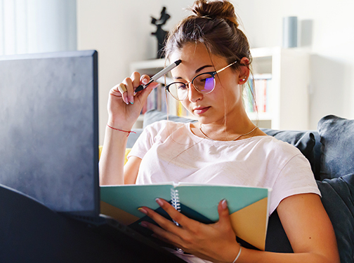 Student studies with laptop and notebook for midterm exams.