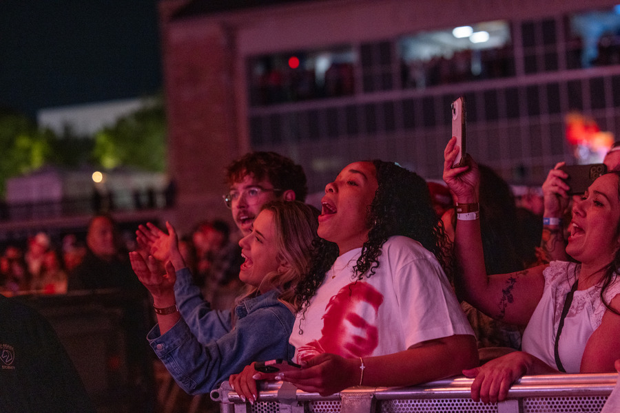 Excited fans cheering at a Zach Bryan concert, some recording with phones.