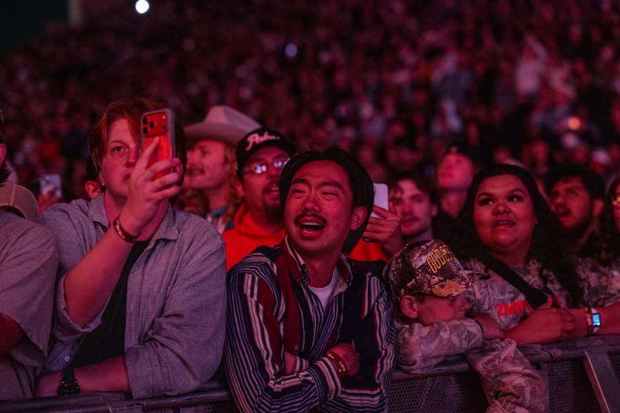 Excited fans at a Zach Bryan concert, some recording with phones, others wearing cowboy hats.