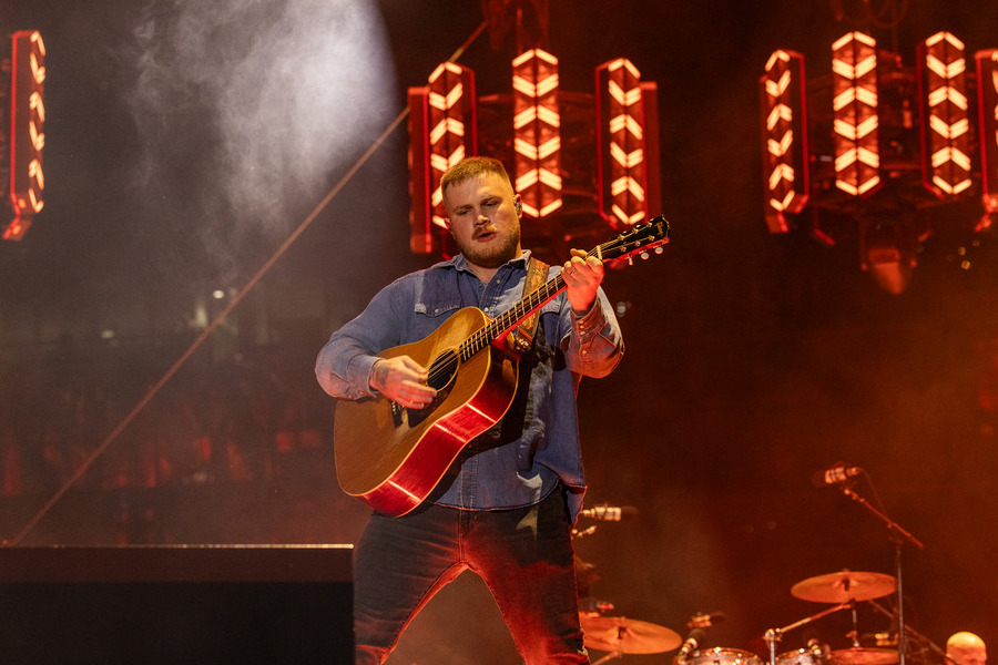 Zach Bryan performing live at a 2026 concert, playing guitar.