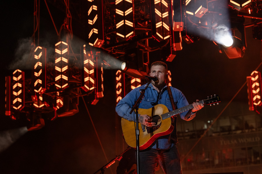 Zach Bryan performs at his 2026 Tulsa concert, playing guitar under stage lights.