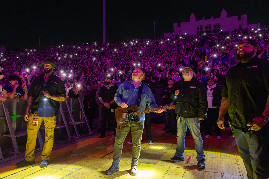 Zach Bryan performs at a packed stadium concert in 2026, fans holding up lights.