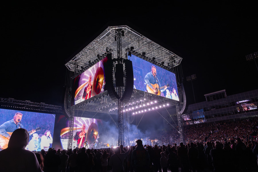 Zach Bryan concert: Large screens show singer on stage to a huge crowd.