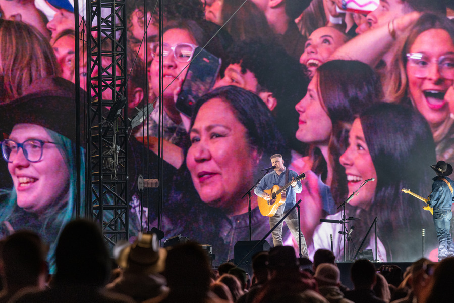 Zach Bryan performs at 2026 concert with fans on screen behind him.