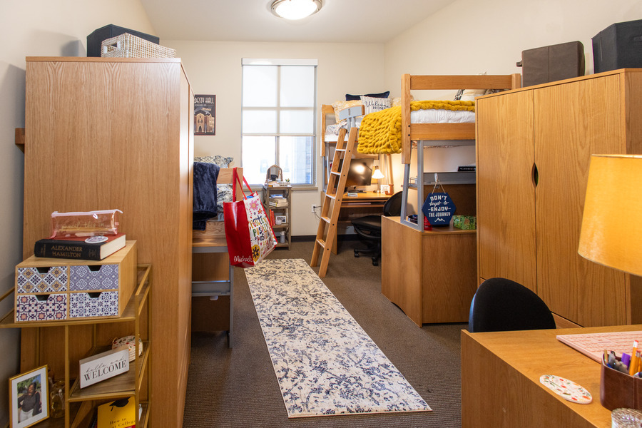 Hardesty Hall dorm room with a loft bed, desk, wardrobes, and a runner rug. Bright, organized student living space.