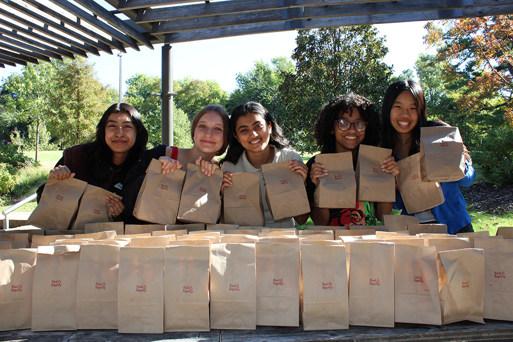 UTulsa students holding "Food Equity" lunch bags outdoors.