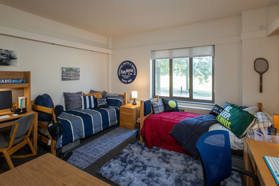 John Mabee Hall dorm room with two beds, desks, and Ford Motor sign.