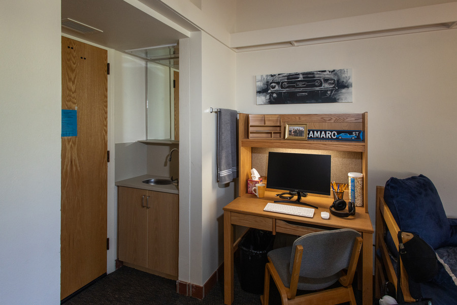 John Mabee Hall dorm room featuring a desk, computer, and private sink area.