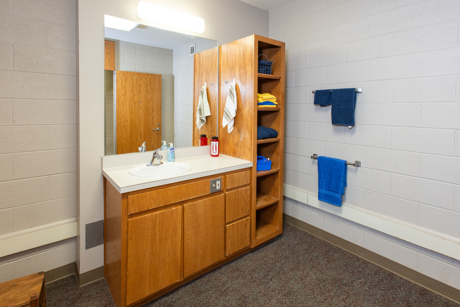 Bathroom in UTulsa's LaFortune House, featuring a sink, mirror, and storage shelves.