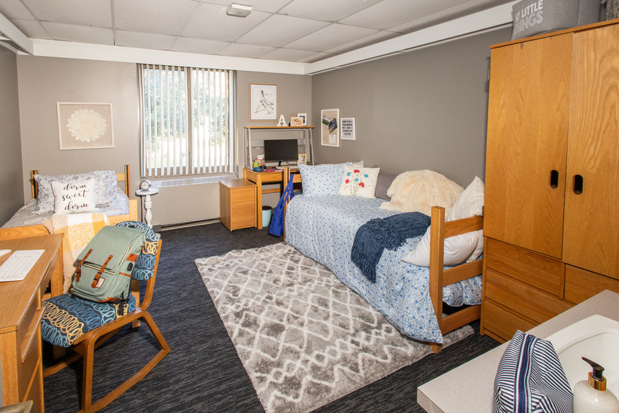 Lottie Jane Mabee Hall dorm room with two beds, desks, a rug, and a wardrobe.