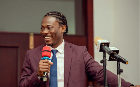 Ghanaian MBA student speaks at podium with microphones, discussing community enrichment.