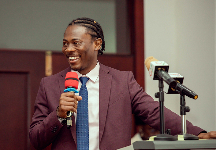 Ghanaian MBA student speaks at podium with microphones, discussing community enrichment.