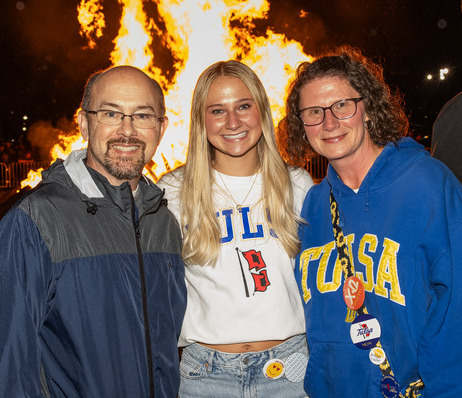 Family posing in front of a bonfire at UTulsa homecoming