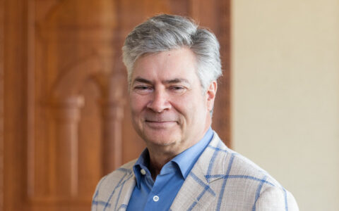 Professional headshot of a man in a blue shirt and plaid blazer smiling.