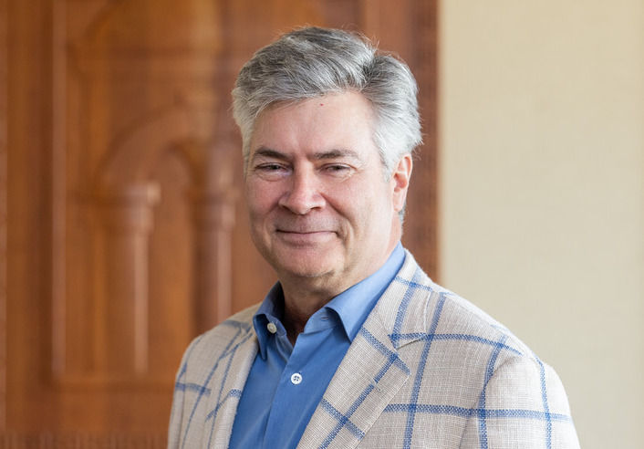Professional headshot of a man in a blue shirt and plaid blazer smiling.
