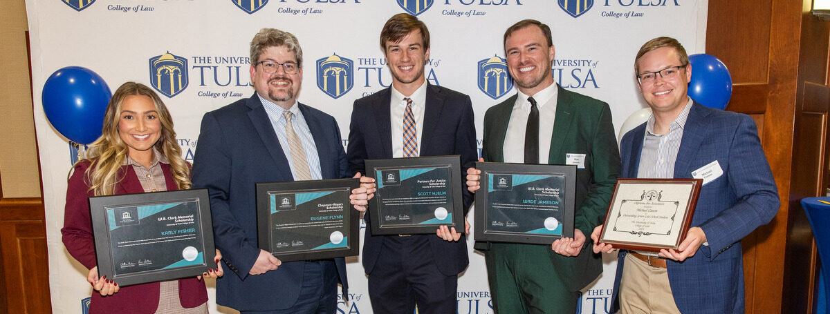 TU Law alumni receive scholarships and awards at a ceremony with the University of Tulsa logo background.