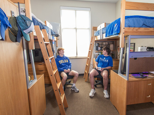 Two male students in a college dorm room with bunk beds, discussing honors opportunities.