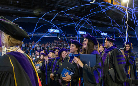 Law graduates in purple robes celebrate at the 2026 Hooding Ceremony with confetti.