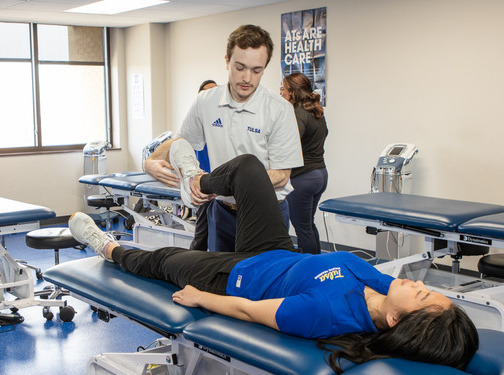 Physical therapist assists patient with leg exercise on a therapy table.