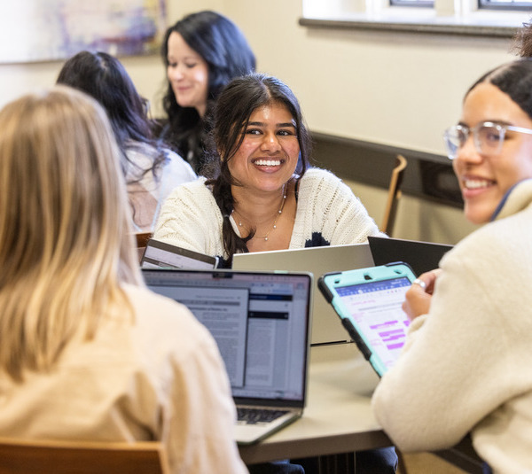 Students using laptops and tablets in a classroom smiling and laughing