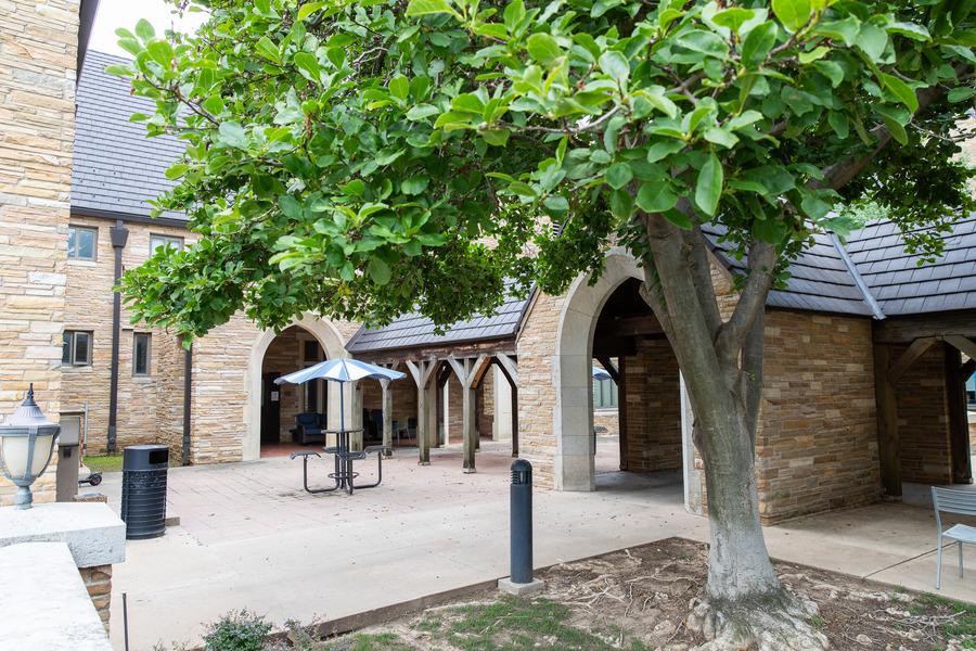 John Mabee Hall courtyard with stone building, arched walkways, and a tree.