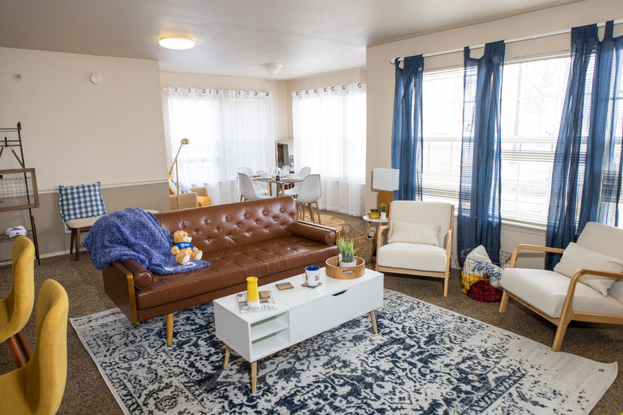 Mayo Village living room with brown tufted sofa, blue rug, and blue curtains.
