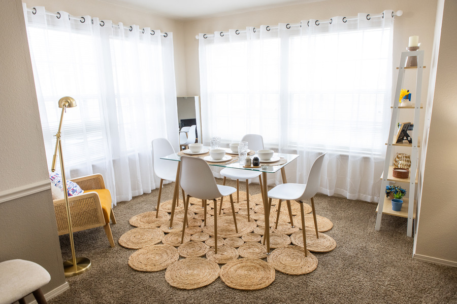 Modern dining area with glass table, white chairs, and straw rug in Mayo Village.