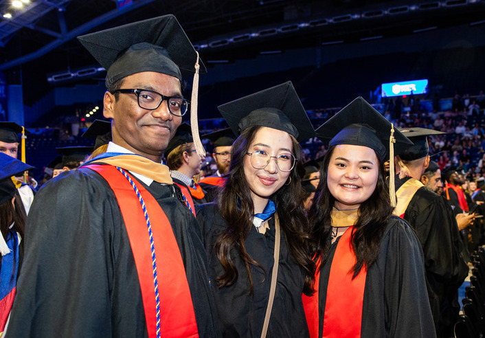 Three 2026 graduates in caps and gowns with red sashes at UTulsa commencement.