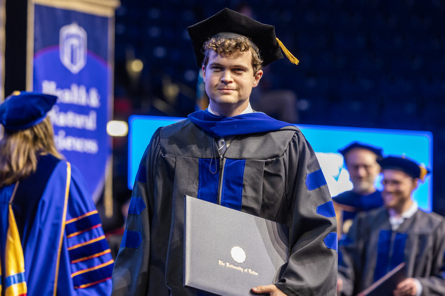 University of Tulsa graduate in academic regalia holding diploma at Commencement 2026.