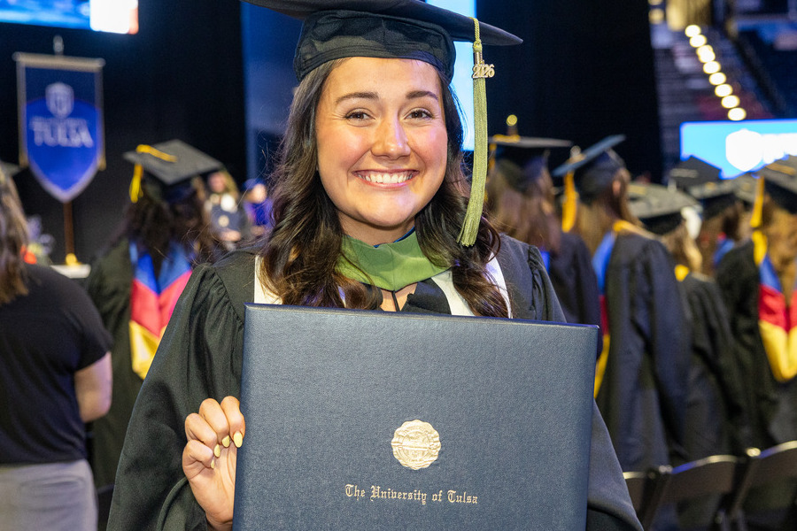 The University of Tulsa graduate smiles holding her diploma at Commencement 2026.