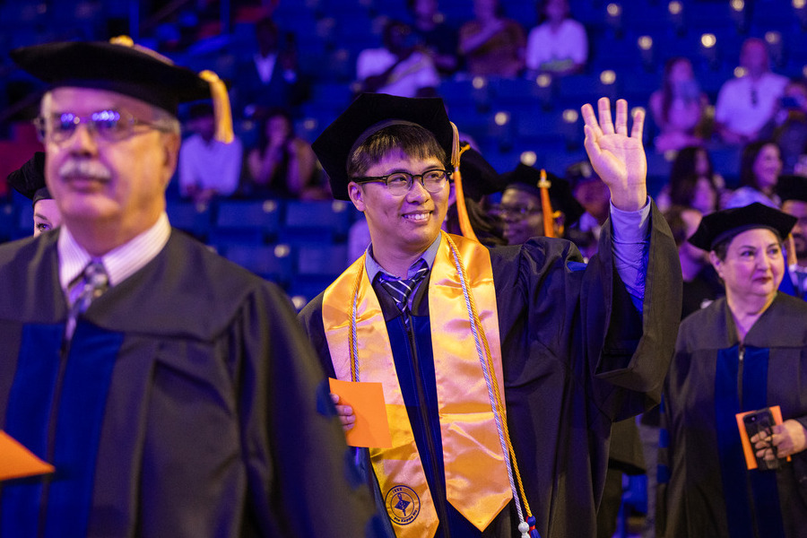 Graduates in caps and gowns at Commencement 2026, one waving