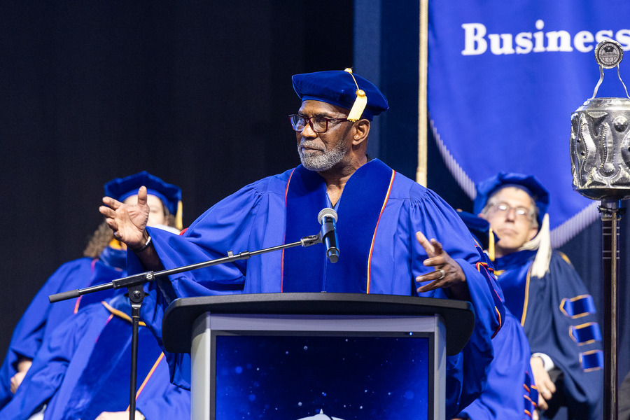 Alumnus Julius Tennon in academic regalia at a commencement podium speaks to graduates.