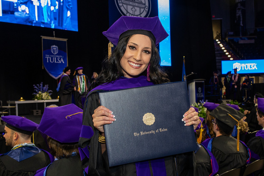 University of Tulsa law graduate smiles holding diploma at 2026 commencement.