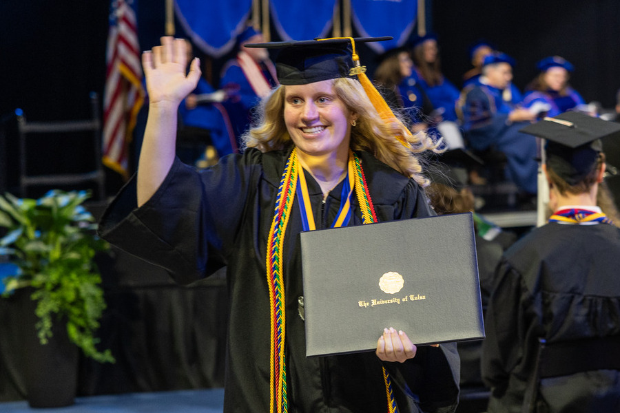 Graduate at commencement 2026 holding diploma and waving, University of Maine.