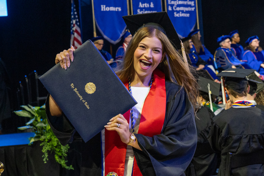 Excited graduate in cap and gown holds diploma at commencement 2026
