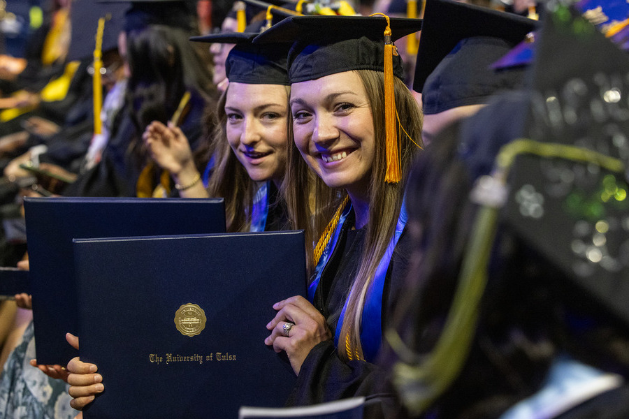 Two smiling graduates in caps and gowns hold diplomas at commencement 2026.