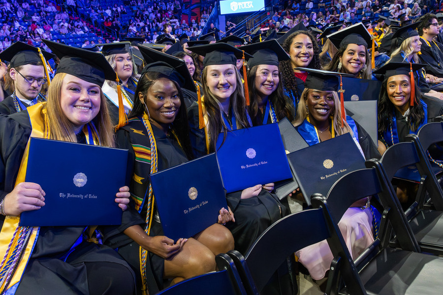 Group of smiling graduates in caps and gowns holding diplomas at commencement 2026.