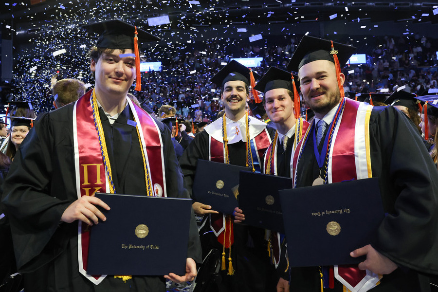 Four smiling graduates in caps and gowns hold diplomas at commencement 2026.